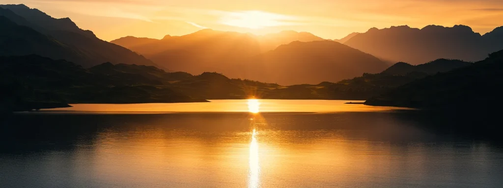 a vibrant sunset casts a golden hue over a serene lake, with silhouetted mountains rising majestically in the background, creating a breathtaking and tranquil landscape.